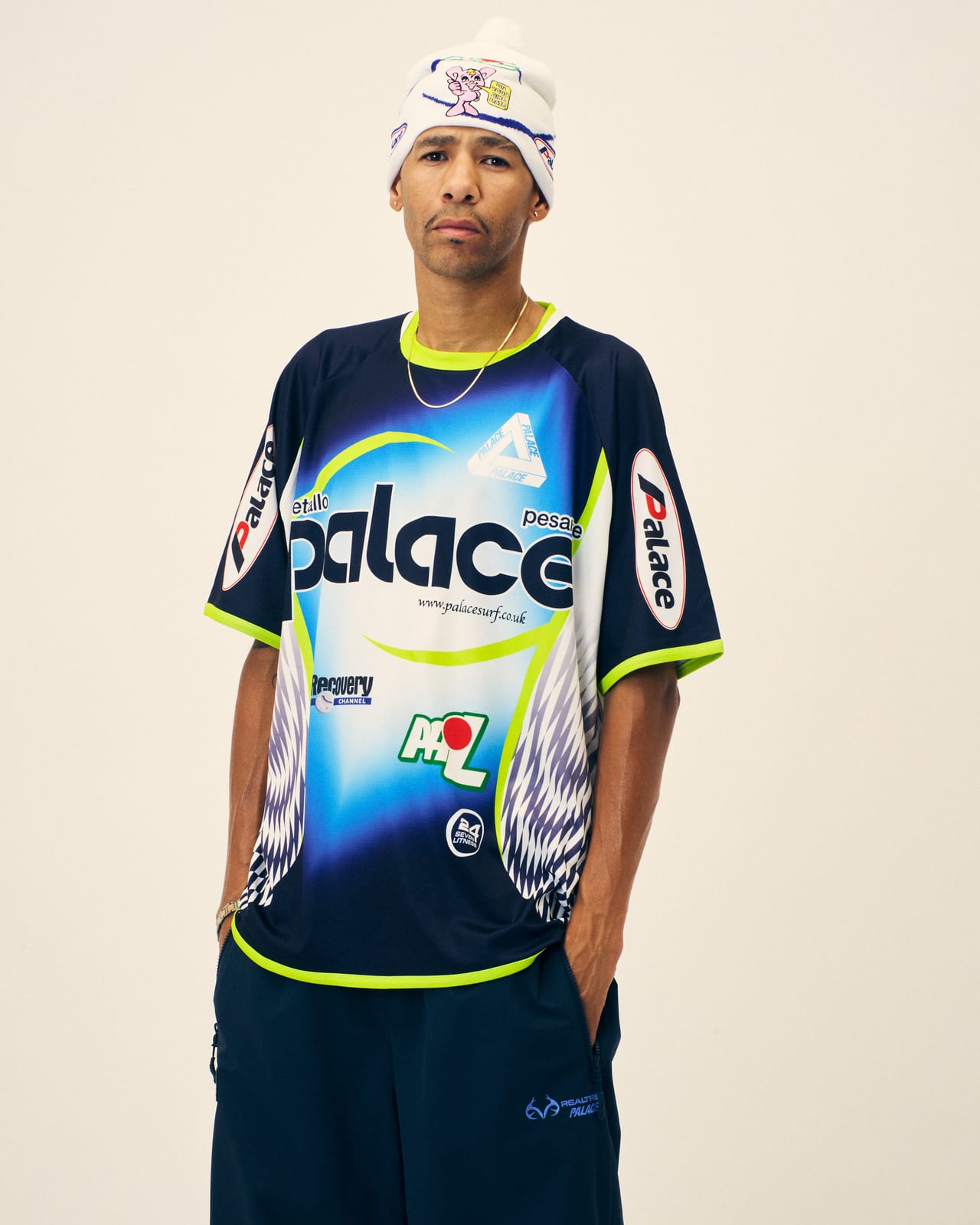 A Palace Winter 2026 mesh racing jersey covered in Palace logos laid out like sponsor patches, worn with a white skull cap