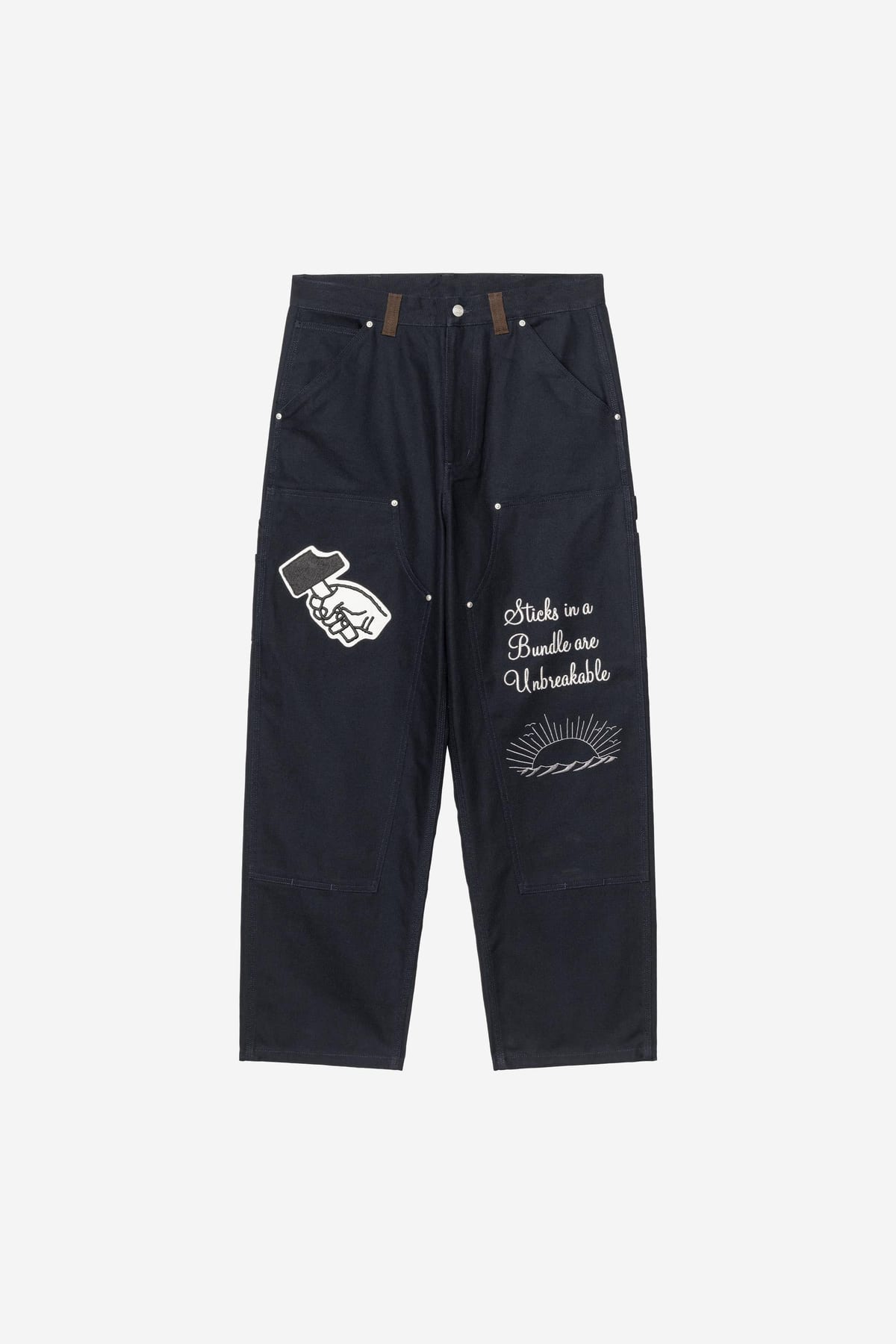 The dark navy Patta x Carhartt WIP OG Double Knee Pant with a patch of a fist gripping a hammer on one leg and 'Sticks in a Bundle are Unbreakable' stitched in white script over a sunrise on the other