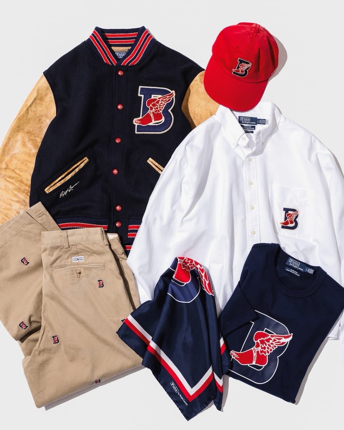 The Polo Ralph Lauren for BEAMS B-WING Collection laid flat: a navy letterman jacket with tan sleeves, a red cap, a white Oxford shirt, khakis, a navy scarf and a navy tee, each with a red winged foot over a navy B