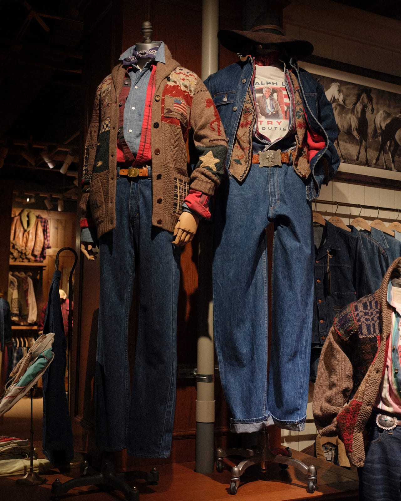 Two mannequins at the PoloFest vintage market in Tokyo, one in a patchwork Americana cardigan with a star patch over a chambray shirt and jeans, the other in a denim jacket over a patterned knit vest and a T-shirt printed with a photo of Ralph Lauren, a large belt buckle and a cowboy hat, beside a rack of denim jackets