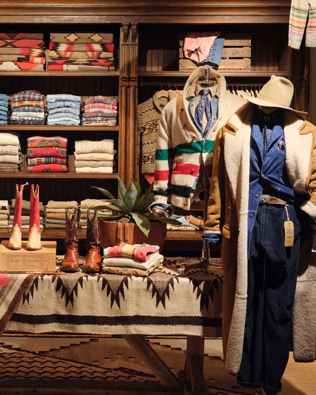 A vintage Polo stall at PoloFest in Tokyo: wooden shelves of folded Southwestern-pattern blankets, flannel shirts and sweaters, red and brown cowboy boots on a patterned table, one pair on a Ralph Lauren Western box, a striped blanket cardigan and a mannequin in a shearling-lined coat, denim and a cowboy hat with a PoloFest vintage tag