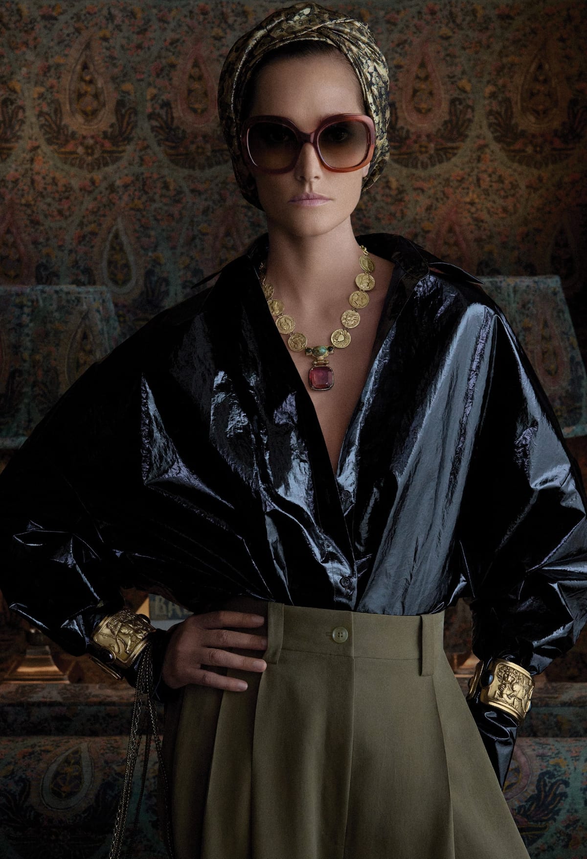 A model in a black shirt and olive trousers wearing the Zodiac Rivière coin necklace and matching gold cuffs