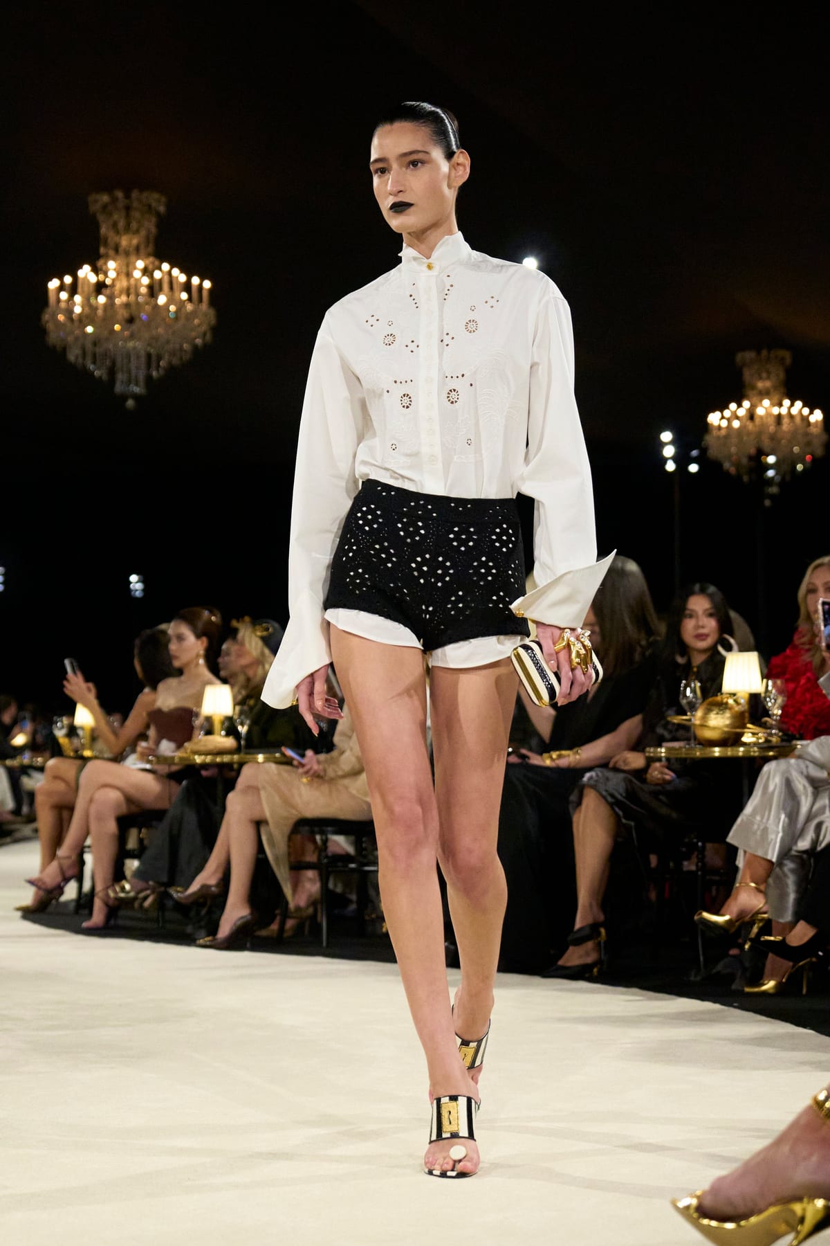 A model in a white shirt with eyelet embroidery and black eyelet shorts, on Schiaparelli's runway