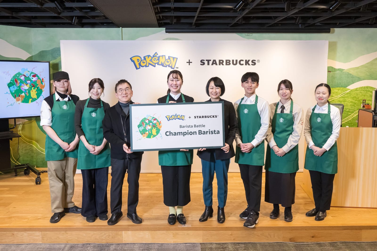 Starbucks Japan staff and the Barista Battle finalists on stage at the Pokémon + Starbucks announcement, holding a Champion Barista board