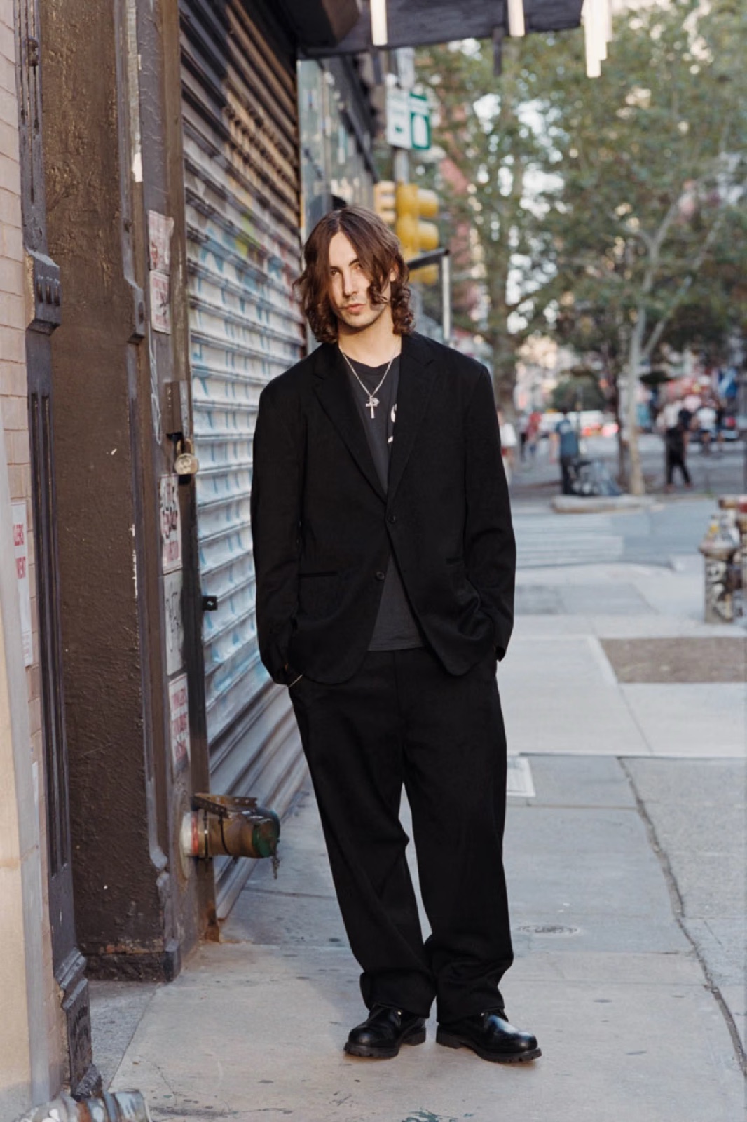 A model in the black cotton-silk suit from Supreme x A.PRESSE, standing on a New York sidewalk