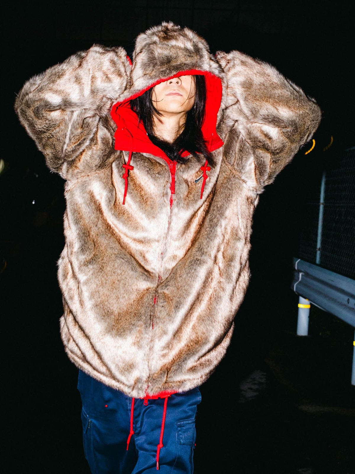 The Supreme x Nike Faux Fur Reversible Parka worn fur side out, with its red-lined hood up, over navy pants