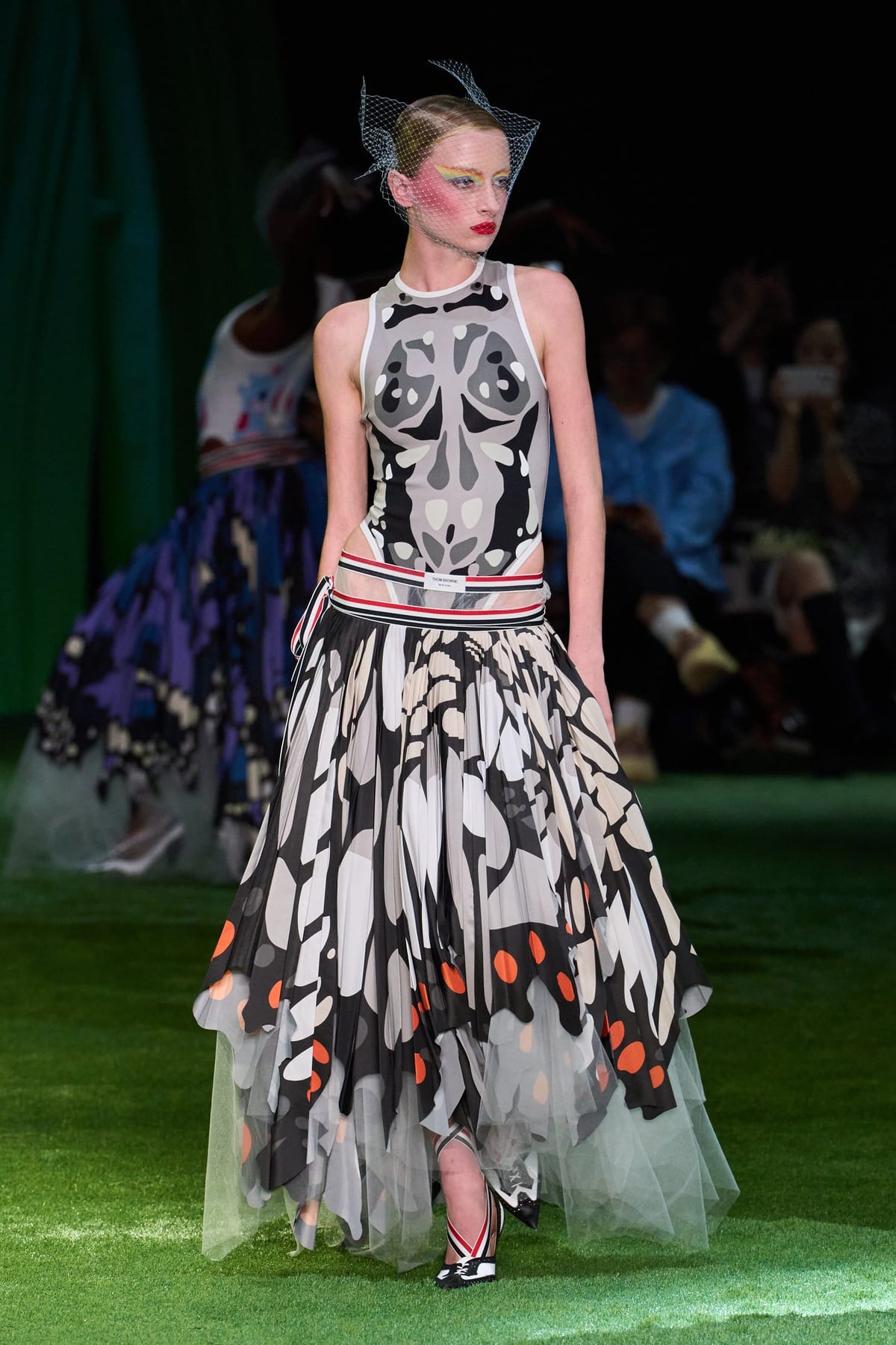 The finale look from Thom Browne's Spring 2027 show: a butterfly-wing print gown in black, grey and orange with a sheer tulle underlayer, worn with a birdcage veil, on an astroturf runway