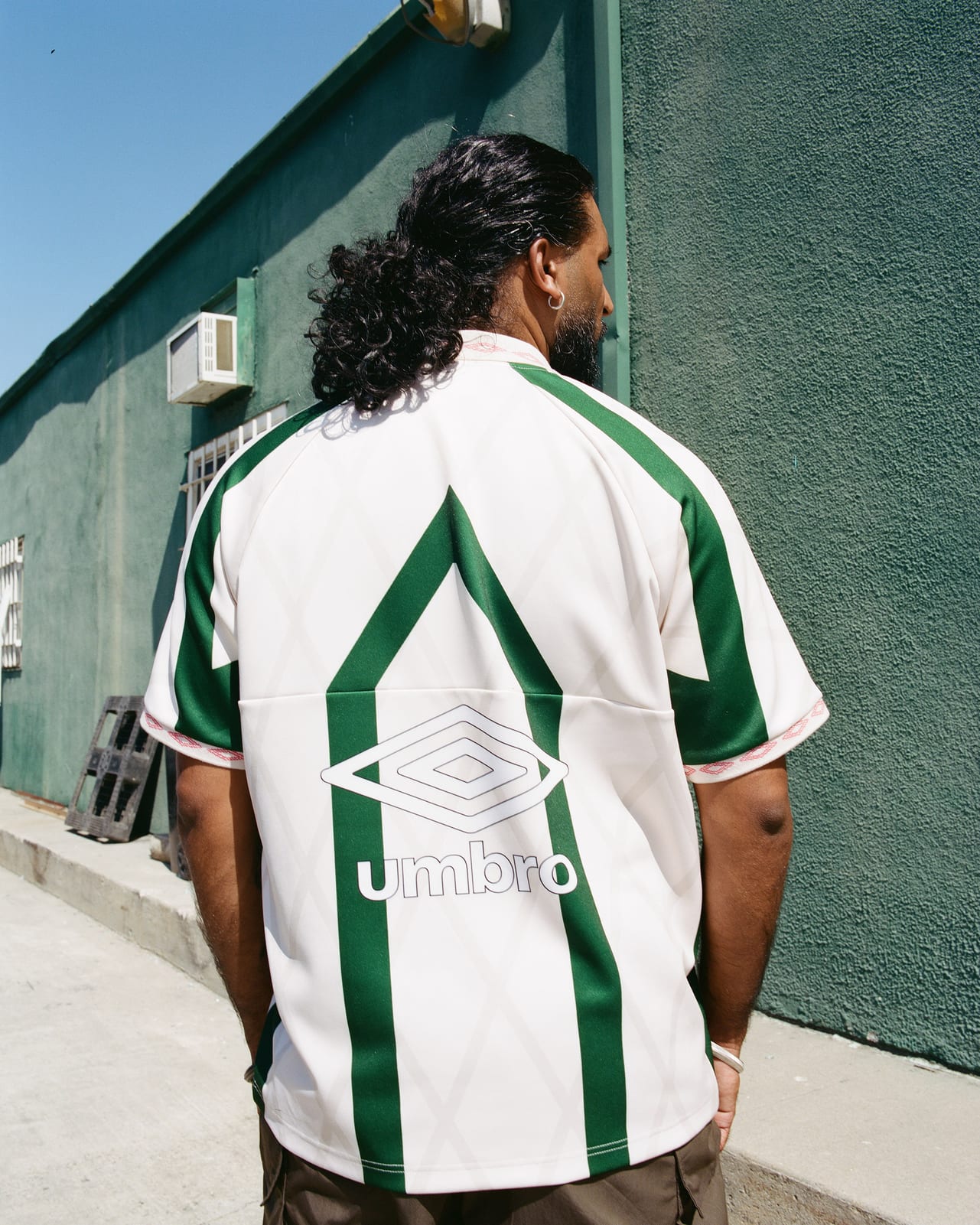 The back of a cream Umbro jersey with wide green stripes, a large green chevron and an Umbro diamond logo, worn with brown cargo pants
