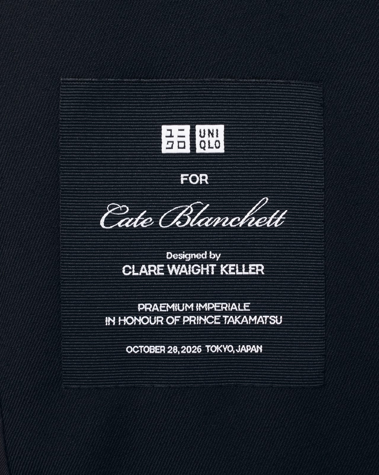 A black grosgrain label with the UNIQLO logo reading: For Cate Blanchett, Designed by Clare Waight Keller, Praemium Imperiale in Honour of Prince Takamatsu, October 28, 2026, Tokyo, Japan