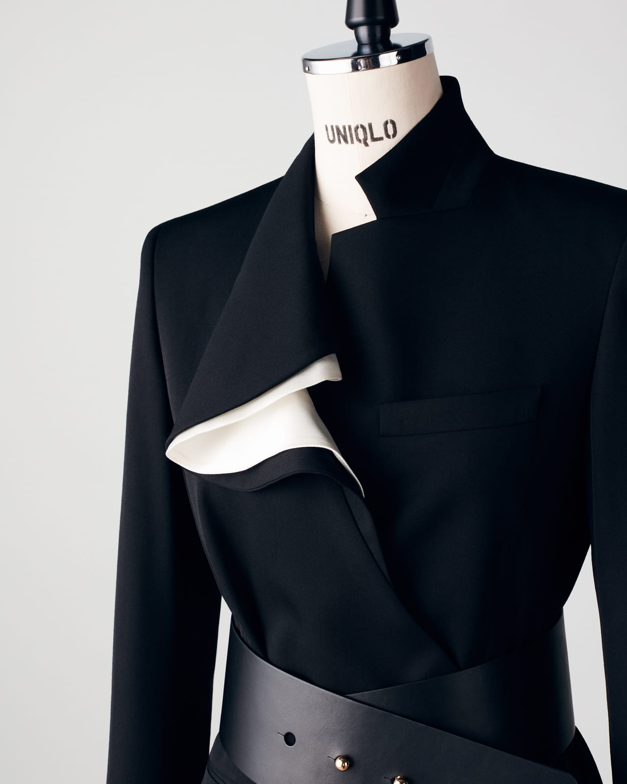Clare Waight Keller's black jacket for Cate Blanchett on a dress form stencilled UNIQLO: a high, folded collar lined in white silk, a welt chest pocket and a wide black leather belt wrapped across the waist